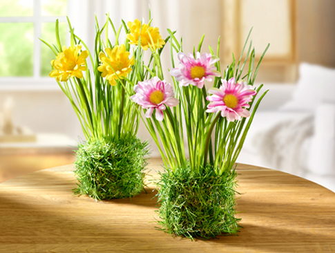 Künstliche Frühlingsblumen in Moosoptik auf Holztisch.